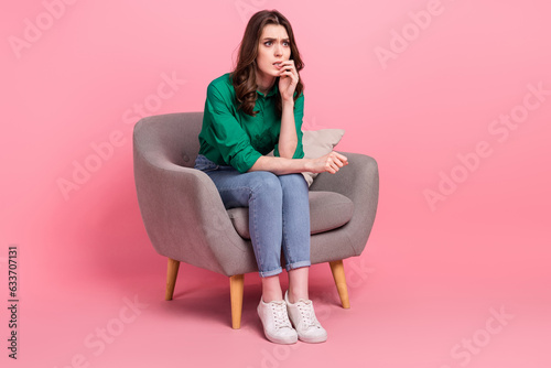 Full length photo of nervous unhappy lady wear green shirt sitting chair looking empty space isolated pink color background