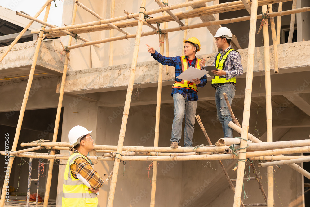 Architects and engineers working together sketching building plans and discussing at construction site wearing uniforms and helmets standing on construction site about large industrial architecture. Architects and engineers working together sketching building plans and discussing at construction site wearing uniforms and helmets standing on construction site about large industrial architecture.