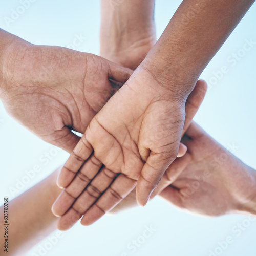Blue sky, hands stack and together for team building motivation, group cooperation or community goals support. Closeup below view, synergy commitment and people collaboration, teamwork and solidarity