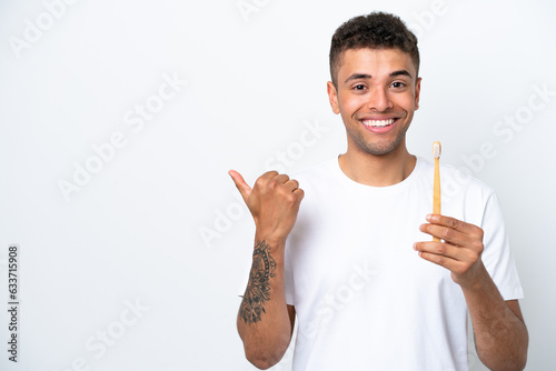 Young Brazilian man brushing teeth isolated on white background pointing to the side to present a product