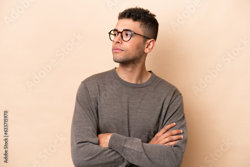 Young Brazilian man isolated on beige background looking to the side