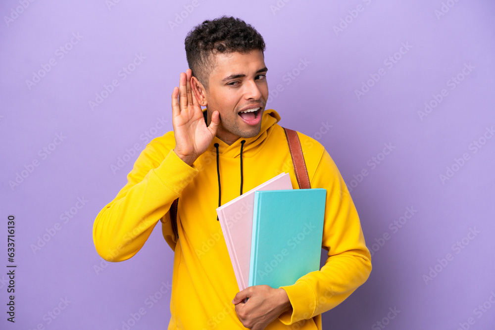 Young student Brazilian man isolated on purple background listening to something by putting hand on the ear Young student Brazilian man isolated on purple background listening to something by putting hand on the ear