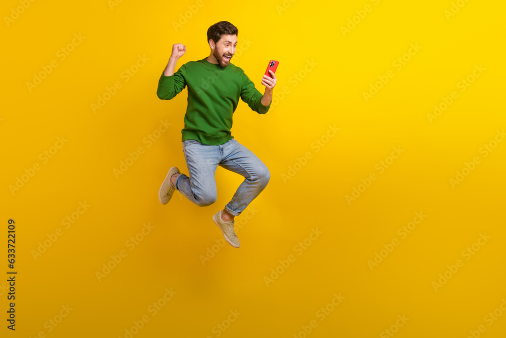 Full length photo of jumper crazy man sales manager fist celebrate his project make profit hold phone isolated on yellow color background
