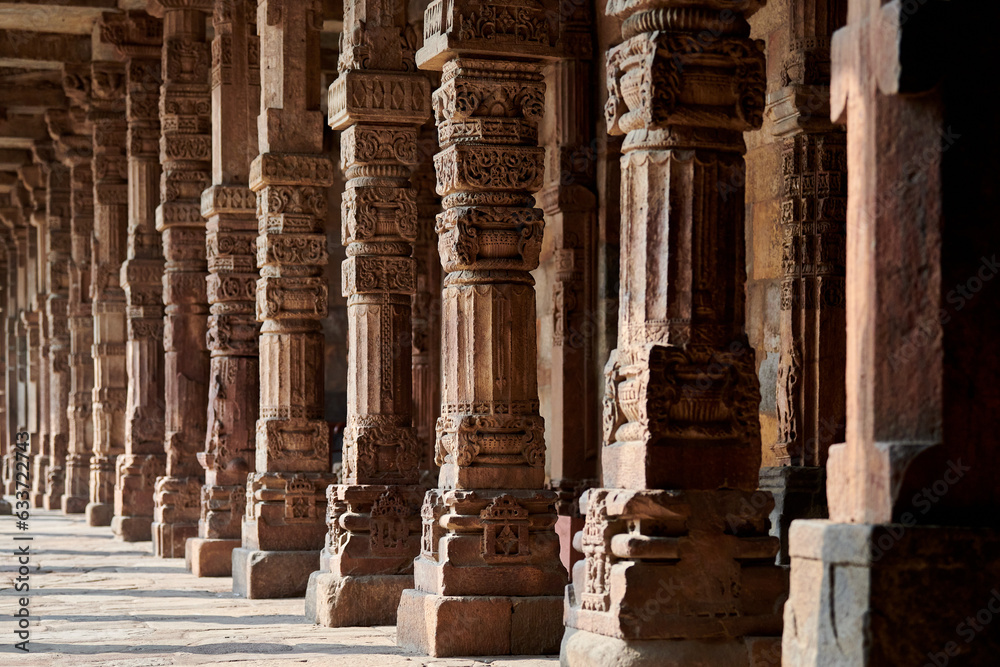 Stone columns with decorative bas relief of Qutb complex in South Delhi, India, close up pillars in ancient ruins of mosque landmark, popular touristic spot in New Delhi, ancient indian architecture