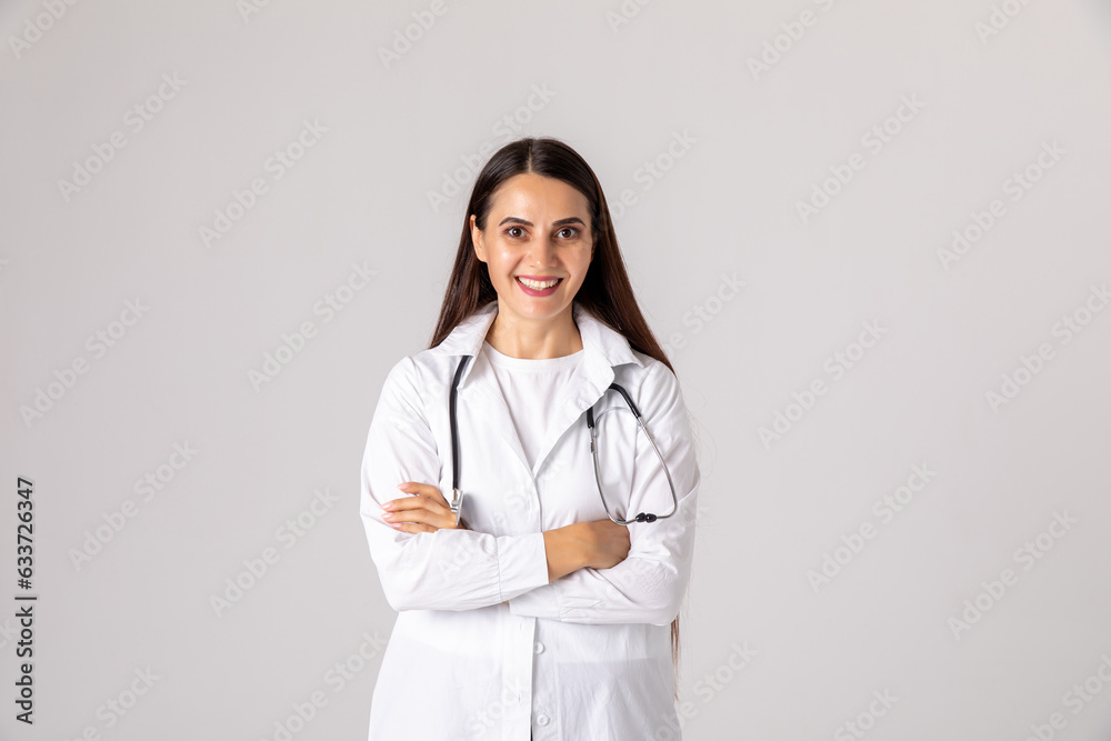 Portrait of beautiful female doctor in white coat looking at camera and smiling while standing with crossed arms on white background Portrait of beautiful female doctor in white coat looking at camera and smiling while standing with crossed arms on white background