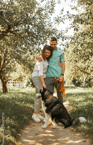 Young happy couple with siberian husky dog in the summer park.