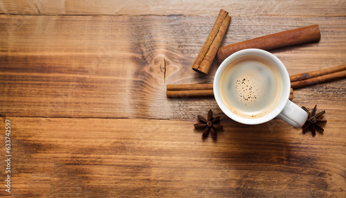 cup of hot coffee with cinnamon and star on a wooden surface, empty space in the middle