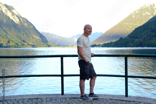 elderly, mature man enjoys morning nature, mountain landscape, lake Achensee in Austria, green mountains rises above calm expanse water, vacation by reservoir, active travel, resort place tyrol © kittyfly