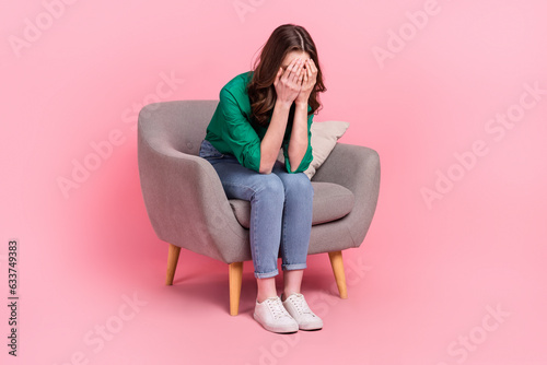 Full size portrait of unsatisfied girl sitting soft chair hands cover eyes crying isolated on pink color background