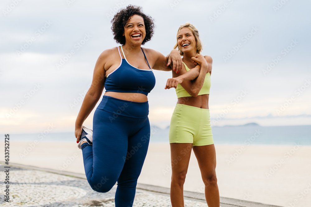 Two happy women doing warm-up exercises on the beach - obrazy, fototapety, plakaty 