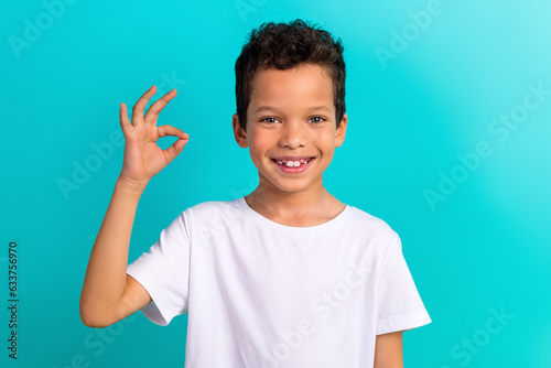 Photo of little cheerful schoolkid toothy smile hand fingers demonstrate okey symbol isolated on teal color background