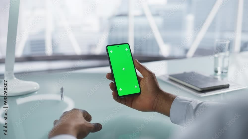 Businessman Holding a Smartphone with Mock Up Green Screen Chromakey Display with Motion Tracker Placeholders. Anonymous Man Sitting Behind a Desk in a Modern Office, Looking at the Phone Screen