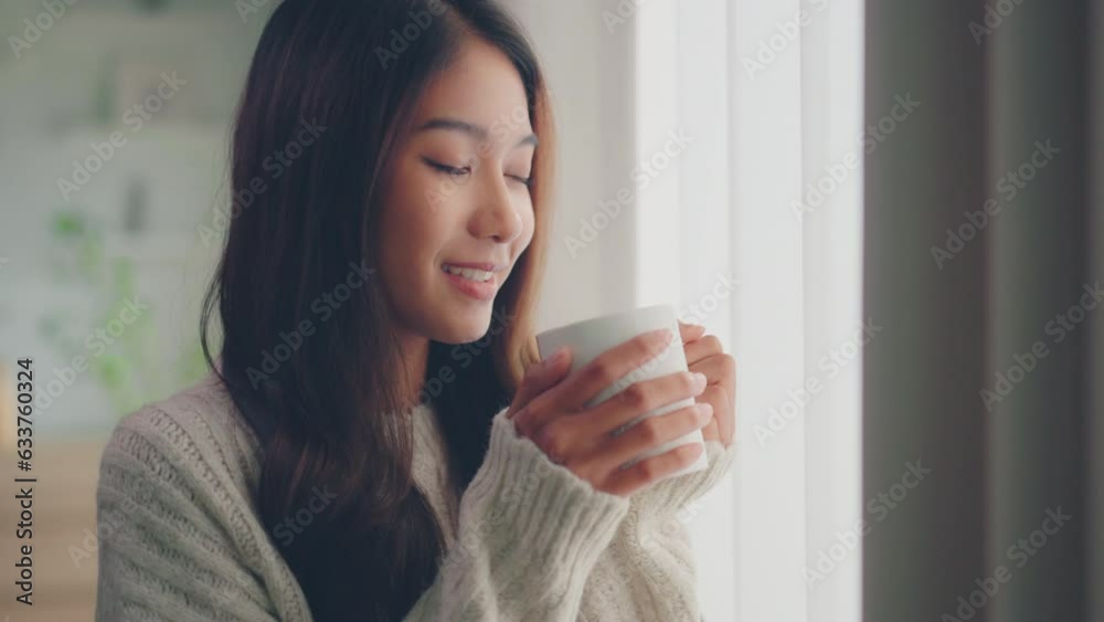Attractive lady enjoying her morning coffee or tea at home, Smiling woman holding cup of tea in hands while looking out the window at morning.