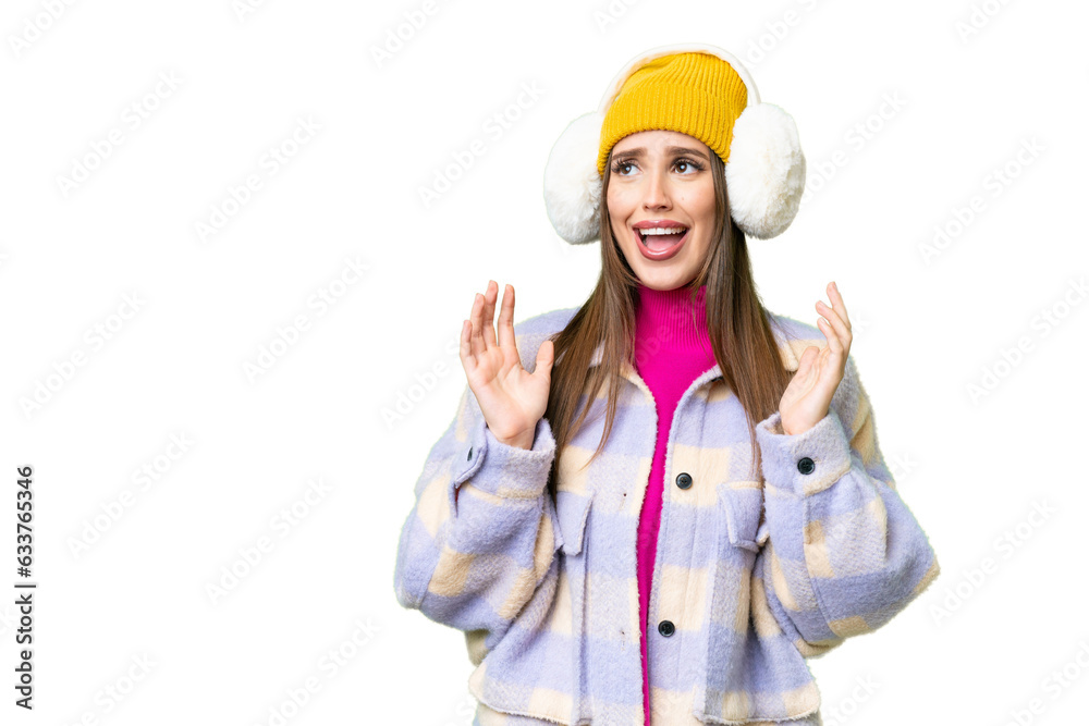 Young woman wearing winter muffs over isolated chroma key background with surprise facial expression Young woman wearing winter muffs over isolated chroma key background with surprise facial expression