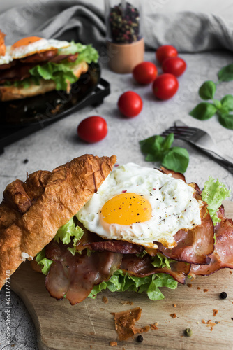 Croissant sandwich with bacon, egg and salad. on wooden board