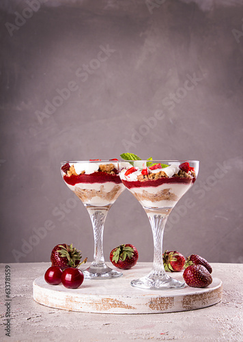 Summer cake in glass, strawberry sweet cherry layered trifle with biscuit, mascarpone and whipped cream on gray background © twomeerkats