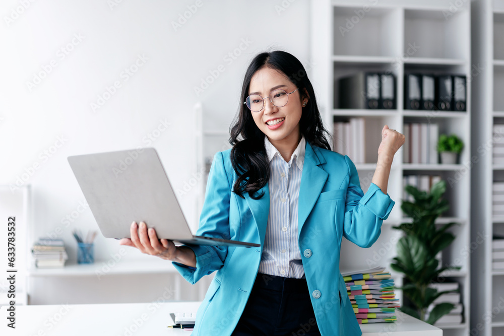 Accounting business concept, Accountant woman reads good news on laptop with excited and raising fist to celebrate achievement while working about investment with business planning finance