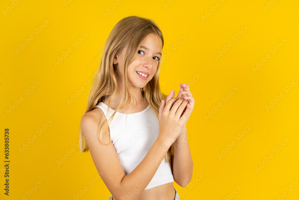 blonde kid girl wearing white T-shirt over yellow studio background clapping and applauding happy and joyful, smiling proud hands together. blonde kid girl wearing white T-shirt over yellow studio background clapping and applauding happy and joyful, smiling proud hands together.