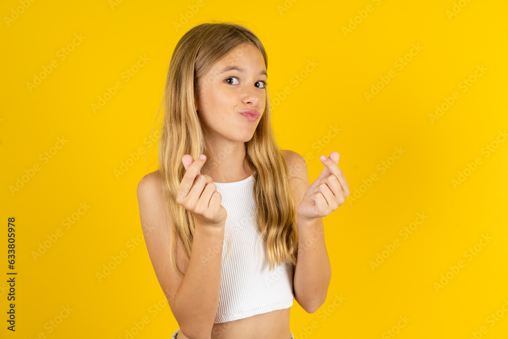 blonde kid girl wearing white T-shirt over yellow studio background doing money gesture with hands, asking for salary payment, millionaire business blonde kid girl wearing white T-shirt over yellow studio background doing money gesture with hands, asking for salary payment, millionaire business