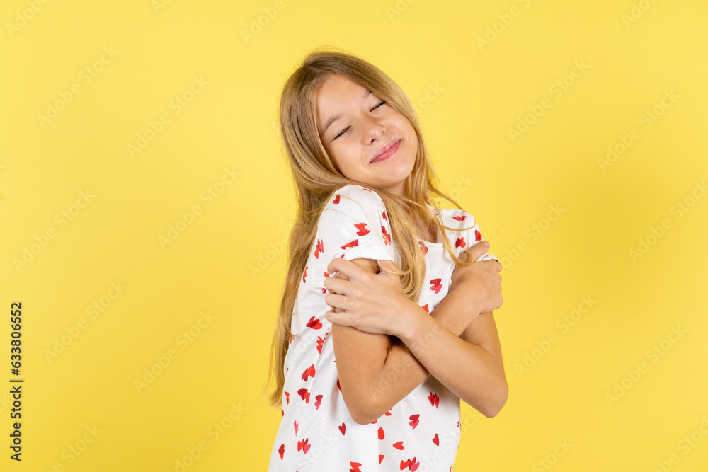blonde kid girl wearing polka dot shirt over yellow studio background Hugging oneself happy and positive, smiling confident. Self love and self care blonde kid girl wearing polka dot shirt over yellow studio background Hugging oneself happy and positive, smiling confident. Self love and self care