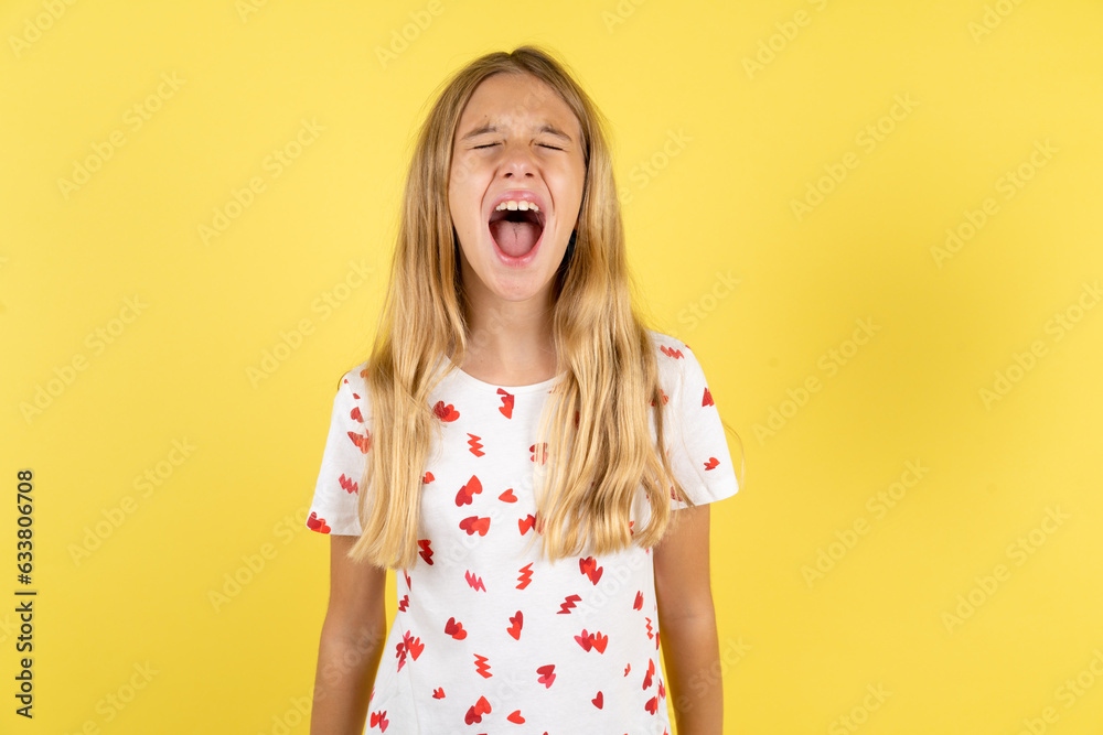 blonde kid girl wearing polka dot shirt over yellow studio background angry and mad screaming frustrated and furious, shouting with anger. Rage and aggressive concept. blonde kid girl wearing polka dot shirt over yellow studio background angry and mad screaming frustrated and furious, shouting with anger. Rage and aggressive concept.