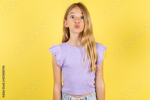 фотографія Shot of pleasant looking blonde kid girl wearing violet T-shirt over yellow stud