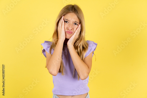 blonde kid girl wearing violet T-shirt over yellow studio background Tired hands covering face, depression and sadness, upset and irritated for problem