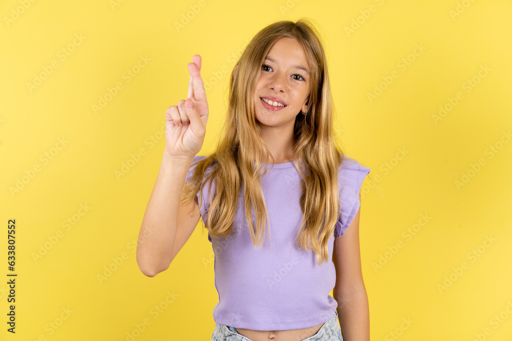 blonde kid girl wearing violet T-shirt over yellow studio background pointing up with fingers number ten in Chinese sign language Shi blonde kid girl wearing violet T-shirt over yellow studio background pointing up with fingers number ten in Chinese sign language Shi