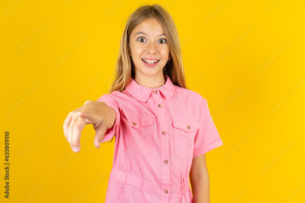 Excited positive young beautiful blonde kid girl over yellow studio background points index finger directly at you, sees something very funny. Wow, amazing Excited positive young beautiful blonde kid girl over yellow studio background points index finger directly at you, sees something very funny. Wow, amazing