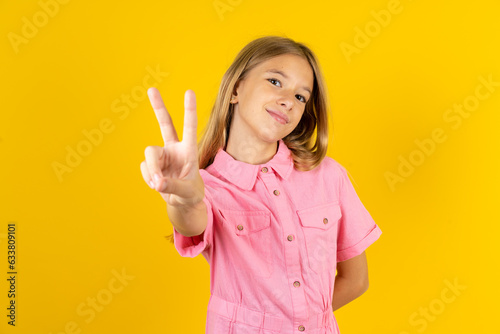 young beautiful blonde kid girl over yellow studio background directs fingers at camera selects someone. I recommend you. Best choice