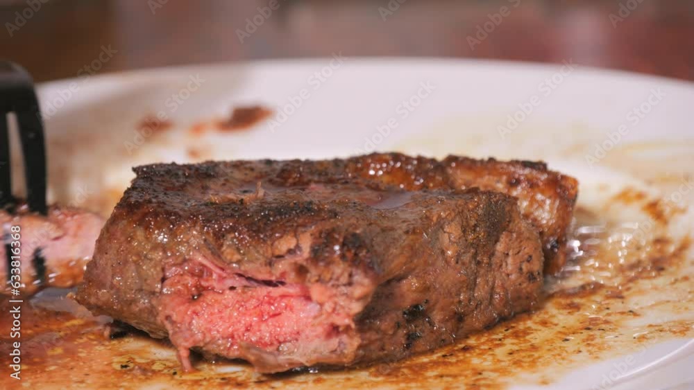 A large piece of freshly grilled beef steak on a plate. Medium-roasted meat with blood in slow motion. A knife and fork cut a piece close up view. A large piece of freshly grilled beef steak on a plate. Medium-roasted meat with blood in slow motion. A knife and fork cut a piece close up view.