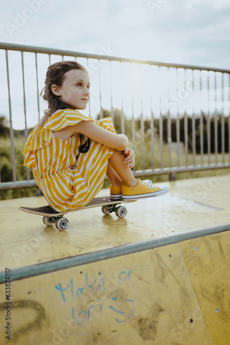 Mädchen, 9 Jahre, im gelbweiß gestreiften Jumpsuit mit Skateboard auf einer gelben Skaterbahn photo