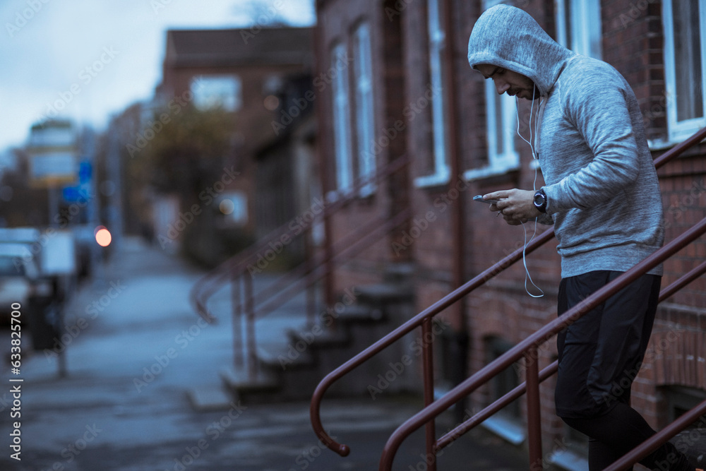 Young man using a smart phone before jogging and exercising on a sidewalk in the city Young man using a smart phone before jogging and exercising on a sidewalk in the city