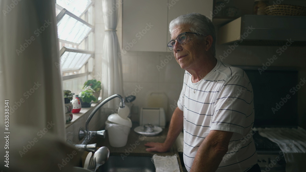 Thoughtful Senior Man Gazing Out of Kitchen Window, Leaning on Counter. Retired older person thinking while staring out window Thoughtful Senior Man Gazing Out of Kitchen Window, Leaning on Counter. Retired older person thinking while staring out window