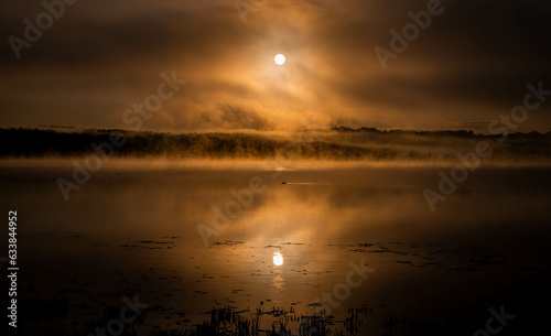sunrise in the middle of the mountains with a orange sun, and lake with blue water. Cloudy morning  © Santiago