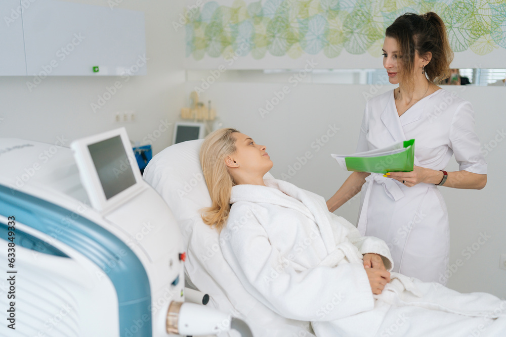 Front view of professional female cosmetologist consulting blonde young woman before alternative face lifting therapy in modern beauty clinic. Concept of rejuvenating skin, preventing aging. Front view of professional female cosmetologist consulting blonde young woman before alternative face lifting therapy in modern beauty clinic. Concept of rejuvenating skin, preventing aging.