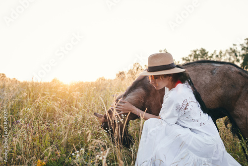 Young woman in the field is walking with goats. The girl and goats in the meadow in summer. Love for animals. Goat farm. Pets. Happy woman with animal. Kindness and love for animals. Kisses a pet.