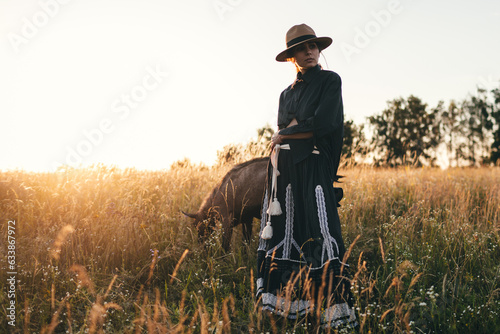Young woman in the field is grazing her white goats. The girl and goats in the meadow in summer. Love for animals. Goat farm. Pets. Happy woman with animal. Kindness and love for animals. Kisses a pet