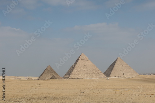 The three pyramids of Egypt side by side in the middle of desert sand with the sky in the background