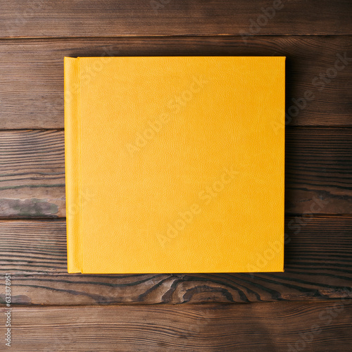 Yellow leather hardcover photobook isolated on a wooden background with copy space. Top view, flat lay. Сlosed book binding mockup for adding personalized text or images.