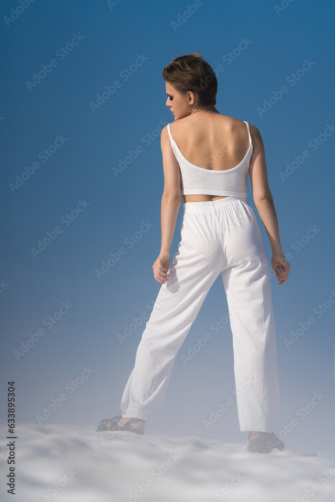Rear view of fashionable woman posing through snow with light fog on sunny day with blue sky Rear view of fashionable woman posing through snow with light fog on sunny day with blue sky