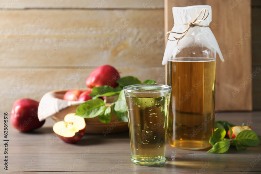 Delicious cider and apples with green leaves on wooden table, space for text Delicious cider and apples with green leaves on wooden table, space for text
