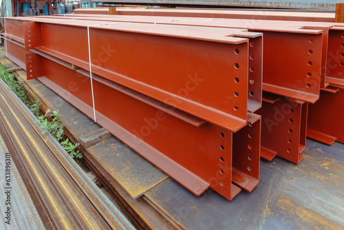 Closeup of red H-beam steel columns, rows of large steel I beams ready for installation at commercial jobs site
