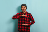 Young Asian man with beanie hat and red plaid flannel shirt gesturing a sign of size with both hands, measuring something, isolated on a blue background