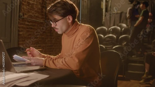 Professional playwright typing on laptop and making notes on papers while working on theater stage. Medium handheld shot