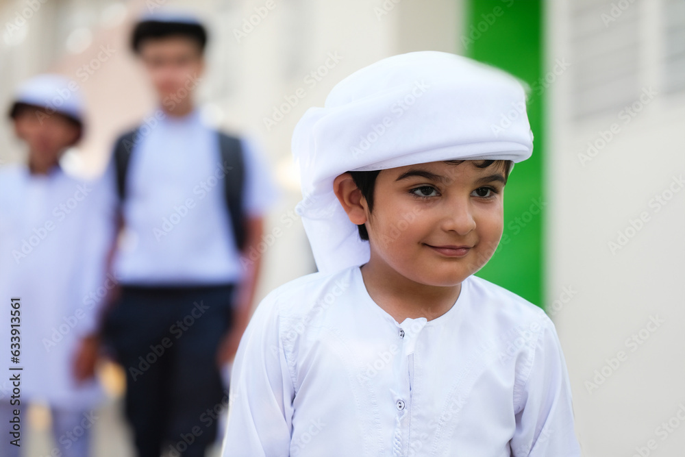 Arab student at school with classmates on the background wearing traditional Kandura Dish dasha for Emirati, Saudi, Qatar, Oman, Kuwait or Bahrain education concept. Happy Arabic boy. Arab student at school with classmates on the background wearing traditional Kandura Dish dasha for Emirati, Saudi, Qatar, Oman, Kuwait or Bahrain education concept. Happy Arabic boy.