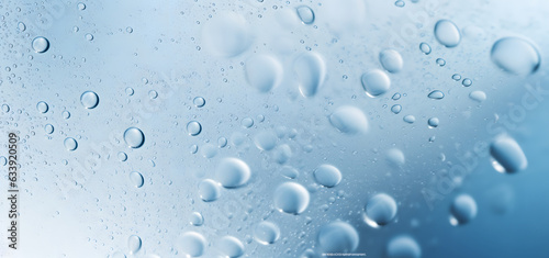 A close-up of clear water droplets scattered on a transparent glass surface with a soft blue background