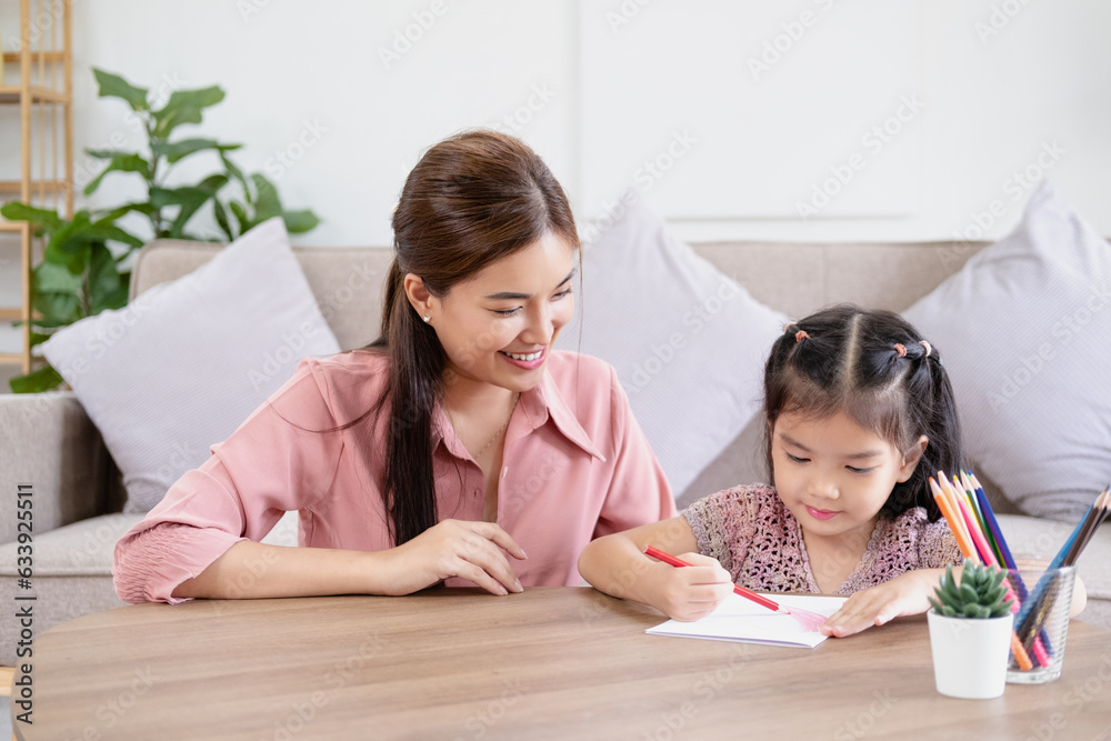 Happy asian girl painting with crayon and colored pencil with his mother in living room at home. Mom teaching daughter how to painting with crayon color on book or doing homework. family concept. Happy asian girl painting with crayon and colored pencil with his mother in living room at home. Mom teaching daughter how to painting with crayon color on book or doing homework. family concept.