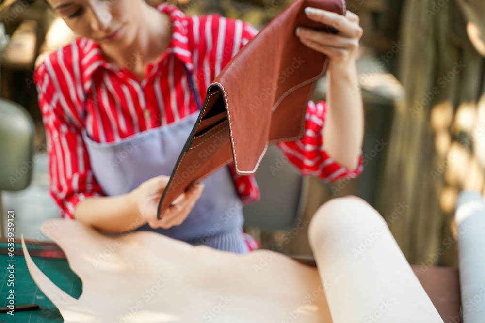 Obraz premium Young female leather goods maker looking and check the neatness of the leathers bag before sell to customer in workshop.