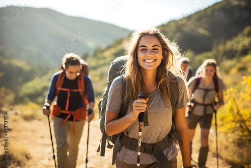 Smiling woman hiker with backpack looking at camera with group of friends hikers rises to the top of the hill
